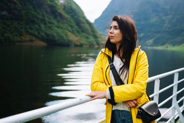 The girl tourist on a pleasure boat on the fjord enjoys the picturesque mountains and lakes of Norway. Young woman posing against the backdrop of the mountains. Travelling, lifestyle, adventure.