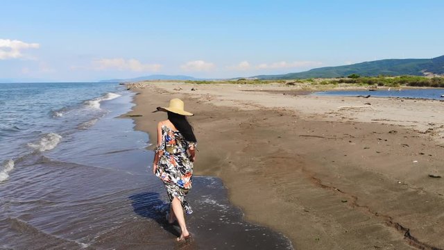 Romantic woman is walking on the beach. Woman dressed in colorful long skirt dress. Waves of the sea are hitting woman’s feet. Alone solo one single emotional sentimental affective sensual emotive. 4K