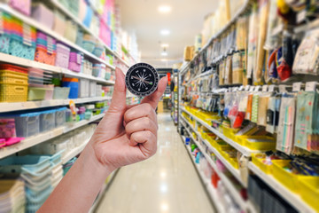 Hand hold compass at supermarket or store background.