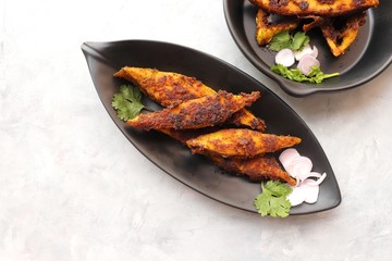 Marinated Pomfret fried fish or Indian Spicy fish fry garnished with onion and coriander on iron skillet griddle, selective focus with copy space.