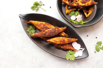 Marinated Pomfret fried fish or Indian Spicy fish fry garnished with onion and coriander on iron skillet griddle, selective focus with copy space.