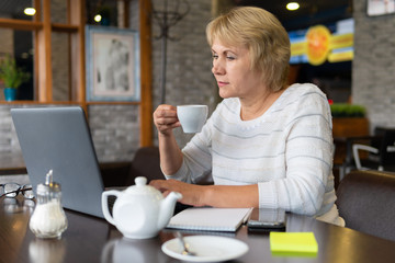 A woman with a laptop looks at a document in a cafe, office