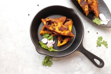 Marinated Pomfret fried fish or Indian Spicy fish fry garnished with onion and coriander on iron skillet griddle, selective focus with copy space.