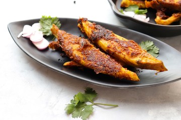 Marinated Pomfret fried fish or Indian Spicy fish fry garnished with onion and coriander on iron skillet griddle, selective focus with copy space.