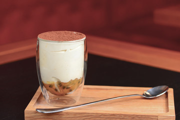 Traditional Italian dessert tiramisu in a glass served on a wooden board with a spoon in a restaurant. Italian cuisine