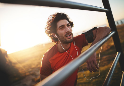 Portrait of a young male athlete enjoying listening to music on his earphones taking a break after running on sunny day