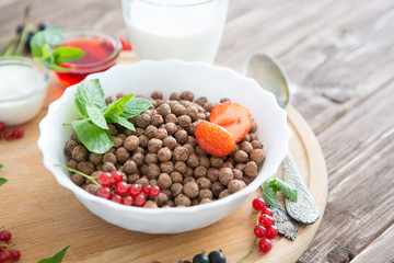 Cereal chocolate balls in bowl with milk on rustic wooden table Healthy tasty breakfast chocolate balls with strawberries, raspberries, black currants and red currants.