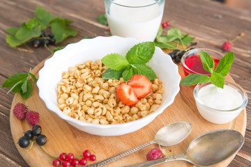 Healthy breakfast with corn flakes, berries, waffle and milk on blue background. Close up. Healthy tasty breakfast of muesli with strawberries, raspberries, black currants and red currants.