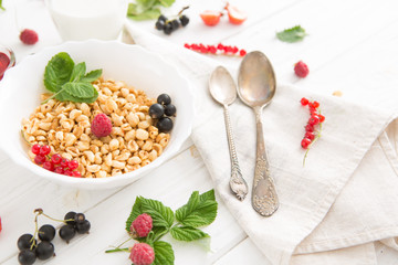Healthy breakfast with corn flakes, berries, waffle and milk on blue background. Close up. Healthy tasty breakfast of muesli with strawberries, raspberries, black currants and red currants.