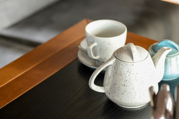 Tea cup with black tea on a small little plate with white tea pot on dark wooden table