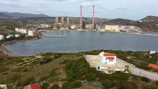 Aerial view of sea bay with old factory and a small white church, low vegetation mountains, Lavrio Greece, move back by drone