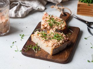 Healthy toasts with salmon pate and fresh green sprouts on yeast-free bread on wood cutting board on grey background. Copy space