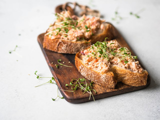 Healthy toasts with salmon pate and fresh green sprouts on yeast-free bread on wood cutting board on grey background.