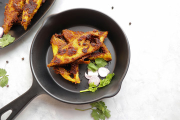 Marinated Pomfret fried fish or Indian Spicy fish fry garnished with onion and coriander on iron skillet griddle, selective focus with copy space.