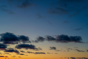 Evening sky at sunset background. Dark clouds hanging above horizon. Majestic cloudscape in blue, orange, violet shades. Grey cloudlets bringing rain. Countryside skyline in twilight time