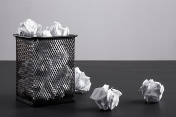 Сrumpled paper balls in a basket on a black office desk on the background gray wall. Office concept.