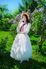 Obraz na płótnie Canvas girl in a white dress and straw hat near flowers hawthorn