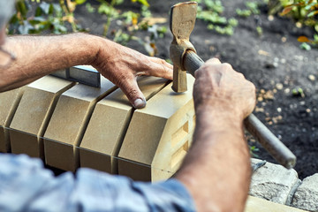 Bricklayer installing bricks on the new fence from facing bricks using hammer.