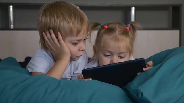 Happy family. A boy and a girl are lying in bed with a tablet in their hands. Communication with peers on social networks. Modern technology at the service of people