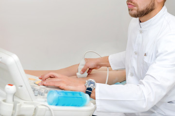 Doctor in white uniform with diagnostic equipment performs an ultrasound using a device on the legs...