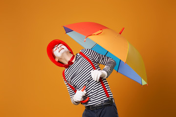 Mime man looking up with multi-colored umbrella in hand isolated on blank orange background