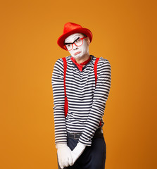 Upset mime man in red hat and vest on orange background