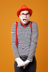 Upset clown mime in red hat and vest on orange background
