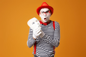 Mime man in red hat and in vest with white mask on orange background