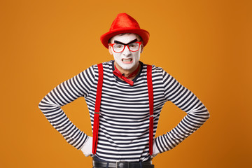 Young mime in white gloves and red hat on orange background