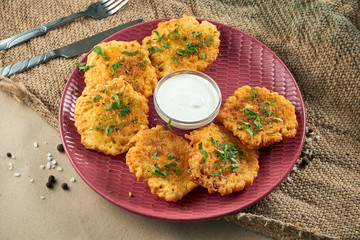 Close up view on Traditional dish of Ukrainian cuisine - potato pancakes with sour cream on a burgundy ceramic plate