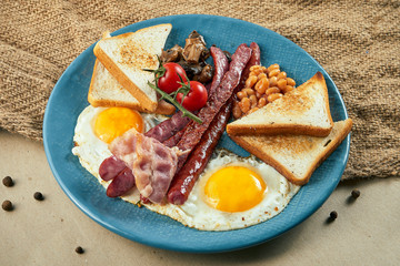 Classic English breakfast: toasts, smoked sausages, bacon, fried eggs, beans and fried toasts on a blue plate. Close up view. Food flat lay