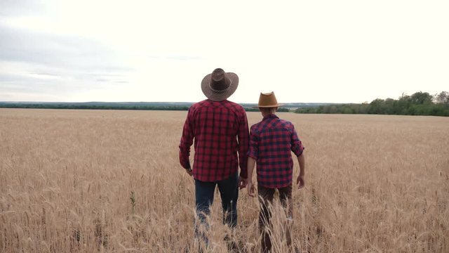 A happy family of farmers is walking through a wheat field. The father puts his arm around his son's shoulder. The way of life in the countryside in the summer.