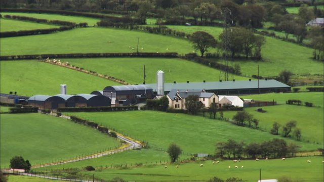 Medium panoramic still shot of countryside farm buildings, lush green livestock grazing fields, and road network, UK, Europe