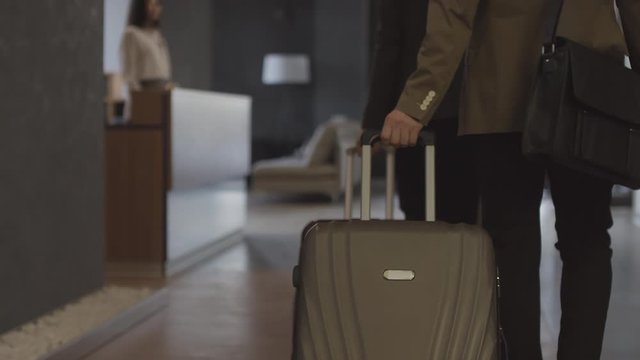 Tracking shot of woman and man with suitcases walking up to reception desk and handing their passports to Asian female receptionist