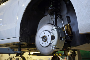 A modern luxury car at a service station is lifted on a lift for repair.  Front brake disc, caliper. Quality after-sales service concept.