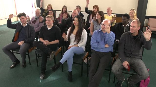 Diverse group of people raising their hands / arms in a meeting or seminar setting. Crane Shot