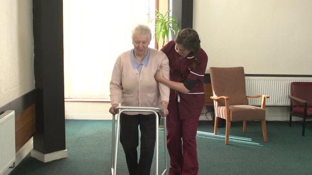 Carer assists an Elderly Senior woman with her Walking Frame / Zimmer frame / Walker