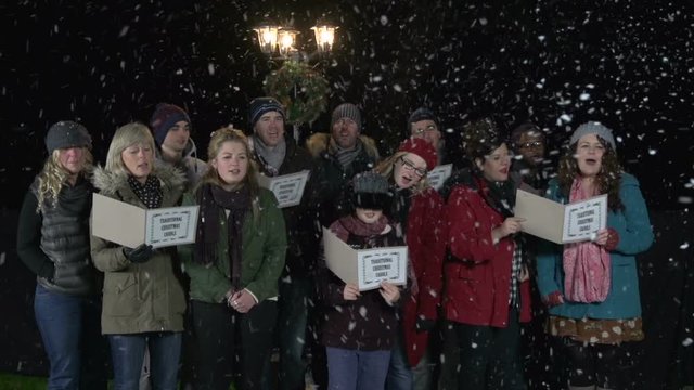 Carol Singers at Christmas Singing outside - Festive scene by lamppost and it's snowing - Stock Video Clip footage