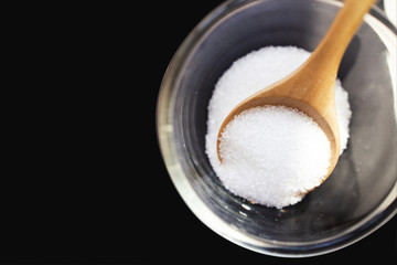 Closeup sugar with a wooden spoon on black background from top view.