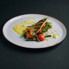 Dorado fillet with green beans, cherry tomato and curry sauce on a black background