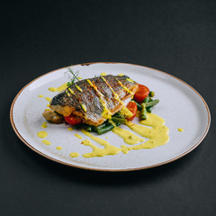 Dorado fillet with green beans, cherry tomato and curry sauce on a black background