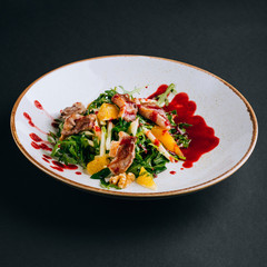 Warm salad with duck breast, orange pulp, arugula, walnuts and cranberry sauce on a black background