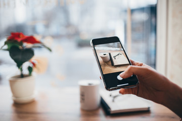 close-up of woman's hands holding a cellphone with empty copy space for your advertising text message or advertising content, hipster girl watching photos on a mobile phone during a coffee break.