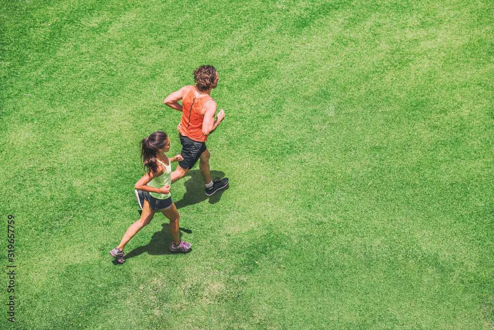 Wall mural jogging couple athletes runners running people on grass park top view from above aerial drone. summe