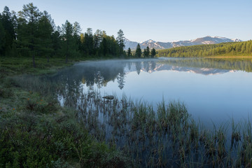 Morning fog on a mountain lake. Dawn in the Altai Mountains.