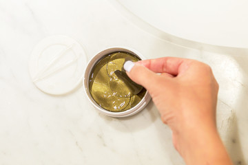 Female hands are taking eye patches out from the container with the tweezers. Anti aging concept