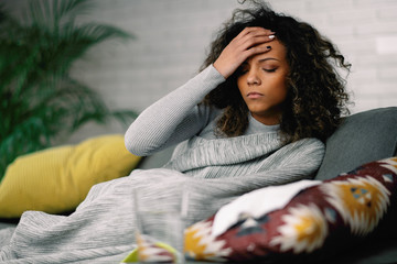 Sick woman at home. Young african woman laying on sofa she is sick having fever. 