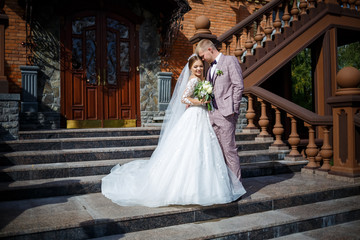 Plakat The bride in a white wedding dress and groom in a suit on the background of a brick building with large steps
