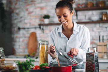 Young woman in kitchen. Beautiful mixed race woman cooking pasta. 