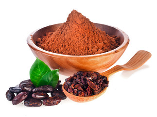 Cocoa powder in a wooden bowl, cacao nibs in a spoon and cacao beans with two leaves isolated on a white background.